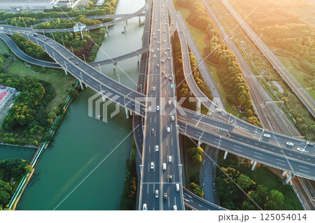 Aerial view of multiple highways intersect above a calm river, surrounded by vibrant greenery. 125054014