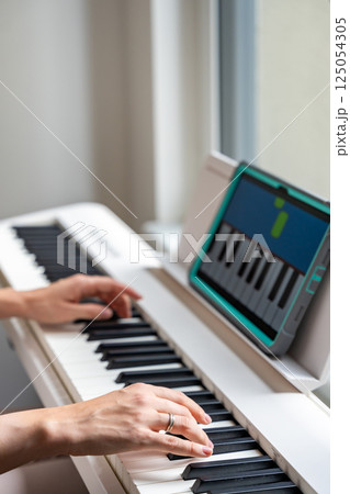 Hands playing a keyboard while following an interactive learning app on a tablet. Technology enables self-education in music without traditional lessons. Hands playing a keyboard while following an interactive learning app on a tablet. Technology enables self-education in music without traditional lessons. 125054305