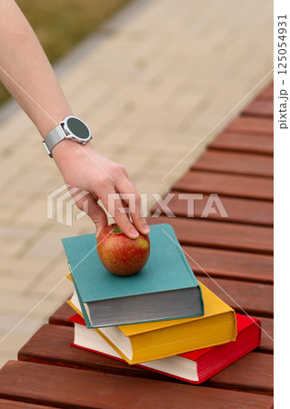 Red apple atop colorful hardcover books held by person's hand. Red apple atop colorful hardcover books held by person's hand. 125054931
