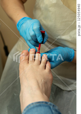 Podiatrist applying red nail polish during final pedicure step 125054940