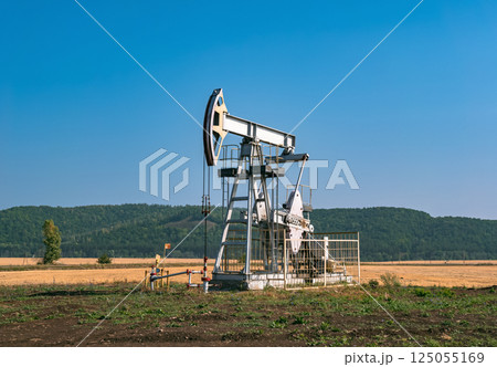 A large oil pump jack operates in an open field, extracting crude oil A large oil pump jack operates in an open field, extracting crude oil 125055169