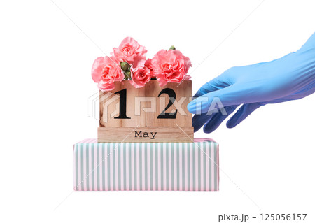 A hand in a blue glove places a wooden calendar showing May 12, isolated on white A hand in a blue glove places a wooden calendar showing May 12, isolated on white 125056157