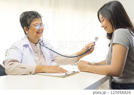 Smiling mature female general practitioner sitting at table and talking to patient Smiling mature female general practitioner sitting at table and talking to patient 125056929