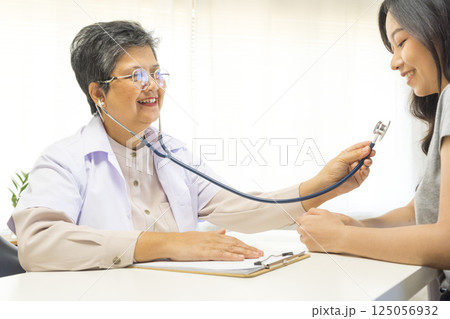 Smiling mature female general practitioner sitting at table and talking to patient 125056932