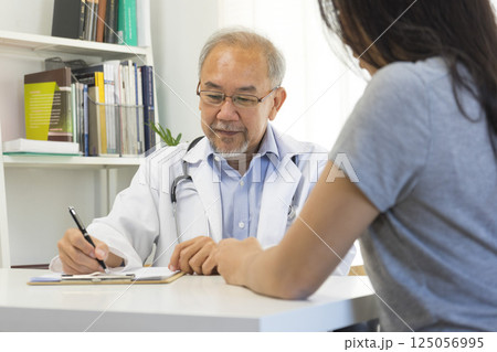 Senior Asian doctor talking with young female patient in hospital. 125056995