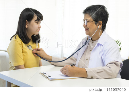 Asian girl and senior psychologist woman having therapy with digital tablet at clinic. Asian girl and senior psychologist woman having therapy with digital tablet at clinic. 125057040