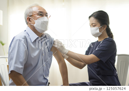 Medical worker perform a vaccine injection to senior Asian man in clinic or medical facility. Medical worker perform a vaccine injection to senior Asian man in clinic or medical facility. 125057624