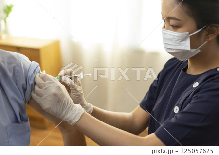 Medical worker perform a vaccine injection to senior Asian man in clinic or medical facility. 125057625