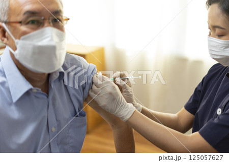 Medical worker perform a vaccine injection to senior Asian man in clinic or medical facility. 125057627