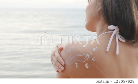 Beautiful Asian woman applying sun protection cream on tanned shoulder on the beach, sun Cream, Close up female in bikini using sunscreen lotion on back body before sunbathing 125057929