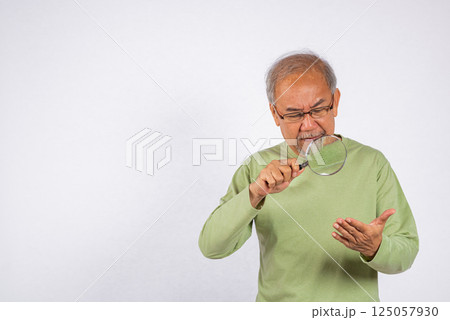 Portrait Asian old man with glasses is looking through a magnifying glass studio shot isolated on white background. senior man use magnifier zoom on hand 125057930