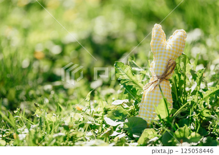Handmade fabric Easter bunnies in yellow and green placed on vibrant green grass under bright spring sunlight Handmade fabric Easter bunnies in yellow and green placed on vibrant green grass under bright spring sunlight 125058446