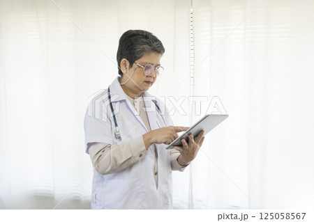 Confident senior female doctor using tablet computer standing in clinic. 125058567