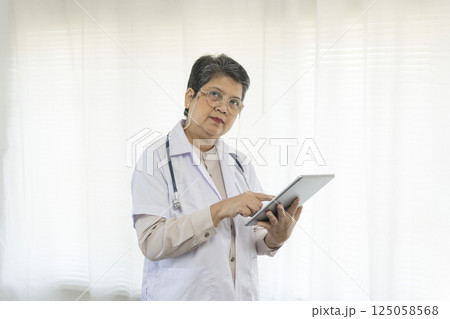 Confident senior female doctor using tablet computer standing in clinic. 125058568