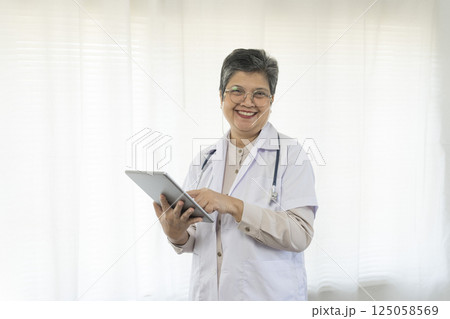 Confident senior female doctor using tablet computer standing in clinic. Confident senior female doctor using tablet computer standing in clinic. 125058569