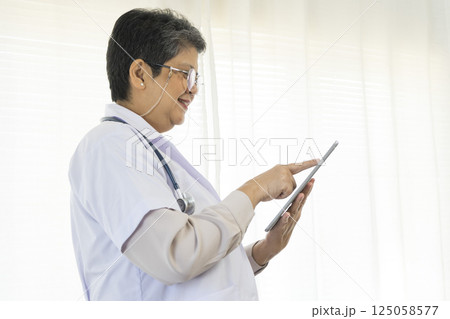 Confident senior female doctor using tablet computer standing in clinic. 125058577