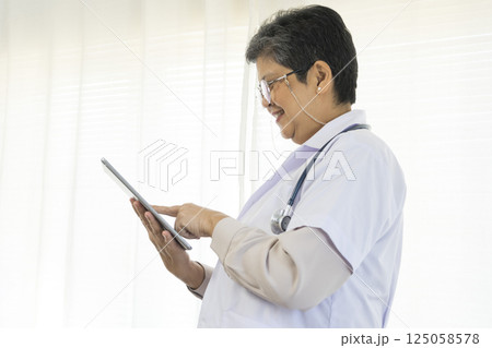 Confident senior female doctor using tablet computer standing in clinic. 125058578