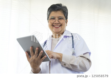 Confident senior female doctor using tablet computer standing in clinic. 125058579