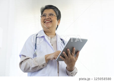Confident senior female doctor using tablet computer standing in clinic. Confident senior female doctor using tablet computer standing in clinic. 125058580