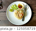 Shrimp fried rice is served on a plate with a spoon, and is seasoned with chili paste and lime. 125058719
