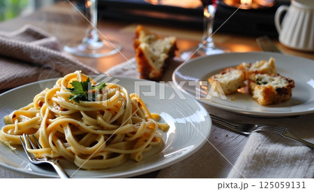 Creamy fettuccine alfredo nestled beside crusty bread slices, candlelight casting soft shadows across elegantly arranged dining surface with romantic atmosphere 125059131