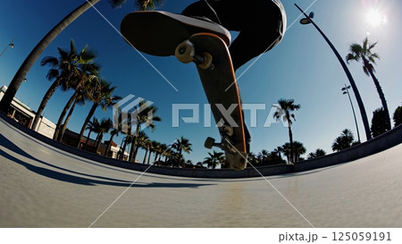 Skilled skateboarder executing aerial tricks at sunny urban skatepark, palm trees framing dynamic movement, highlighting skateboarding expertise with high energy motion capture 125059191