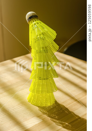 Neon yellow badminton shuttlecock with sharp shadows on sunlit wooden table. High quality photo 125059598