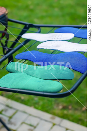 Colorful shoe insoles drying on outdoor metal rack in fresh green garden view. High quality photo 125059604