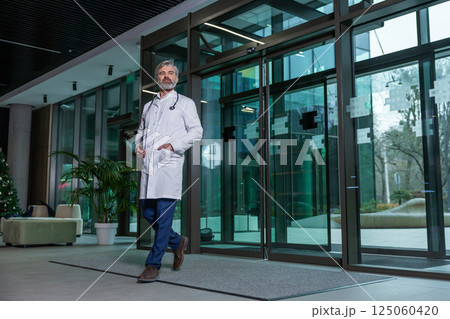 Mature male doctor in lab coat entering the clinic and looking determined 125060420