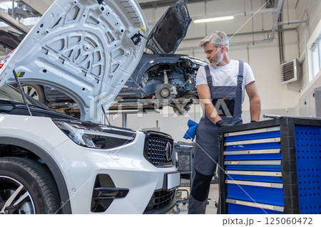 Handyman in auto workshop with equipment for labor work on vehicle repair and diagnostics 125060472