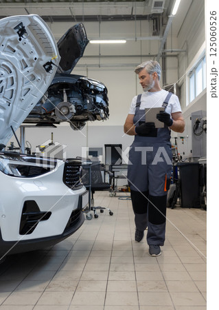 Technician in auto shop using advanced technology for inspection and fixing mechanical parts Technician in auto shop using advanced technology for inspection and fixing mechanical parts 125060526
