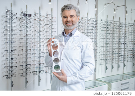 Male doctor in the optic shop holding a lens color scale in hands Male doctor in the optic shop holding a lens color scale in hands 125061179