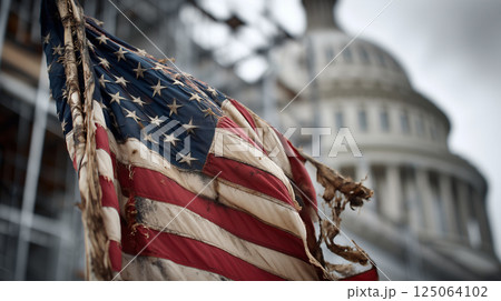 Tattered American flag fluttering against blurred Capitol Building backdrop, symbolizing resilience and national heritage 125064102