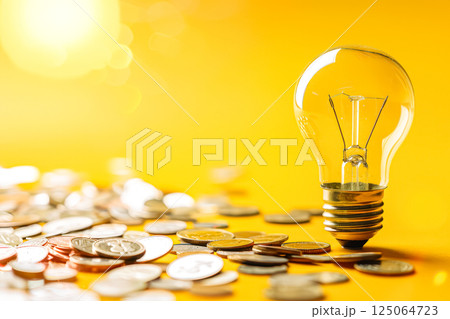 Light bulb is surrounded by a pile of coins Light bulb is surrounded by a pile of coins 125064723