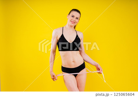 Smiling slim woman measuring her waist with tape. Fit young lady perfect shape, happy with her body Smiling slim woman measuring her waist with tape. Fit young lady perfect shape, happy with her body 125065604