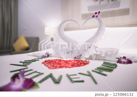 Swans made of towels are a symbol of love and relationships, and a heart made of rose petals on a white bed for lovers in a hotel room in close-up. The Happy Honeymoon inscription is lined with green Swans made of towels are a symbol of love and relationships, and a heart made of rose petals on a white bed for lovers in a hotel room in close-up. The Happy Honeymoon inscription is lined with green 125066132