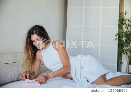 Woman in pajamas opening gift in the morning in the bedroom Woman in pajamas opening gift in the morning in the bedroom 125066593