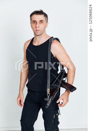 A man in clothes holding a military assault rifle and a weapon A man in clothes holding a military assault rifle and a weapon 125066624