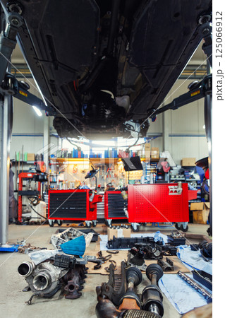 Scenic bottom POV disassembled SUV car with removed gearbox raised on lift elevator at workshop service maintenance station center. Vehicle check-up and repair. Underbody chassis and suspension parts 125066912