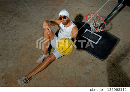 A basketball player sits on the court wearing sunglasses, relaxed after an intense practice session at dusk A basketball player sits on the court wearing sunglasses, relaxed after an intense practice session at dusk 125068312