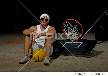 A basketball player sits on the court wearing sunglasses, relaxed after an intense practice session at dusk 125068313