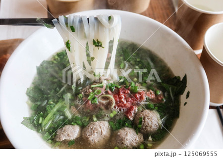 close up of Vietnamese beef pho rice noodles with beef ball and thinly sliced raw beef added to a steaming bowl of savoy broth close up of Vietnamese beef pho rice noodles with beef ball and thinly sliced raw beef added to a steaming bowl of savoy broth 125069555