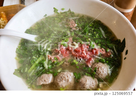 close up of Vietnamese beef pho rice noodles with beef ball and thinly sliced raw beef added to a steaming bowl of savoy broth 125069557