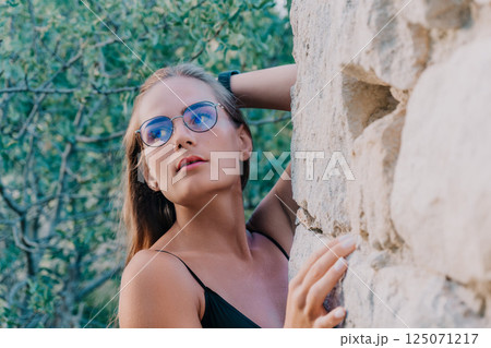 Woman Sunglasses Stone Wall - Portrait of a young woman wearing sunglasses leaning against a stone wall. Woman Sunglasses Stone Wall - Portrait of a young woman wearing sunglasses leaning against a stone wall. 125071217