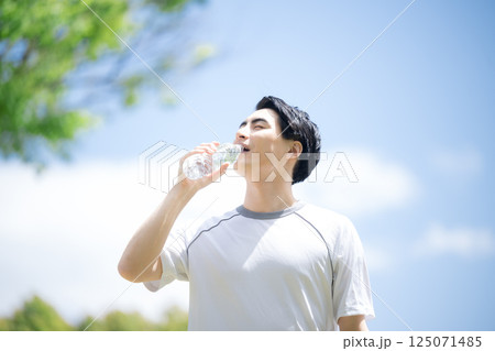 青空の中、ランニングのスポーツや運動で水分補給(水を飲む)する若い男性のクローズアップ 青空の中、ランニングのスポーツや運動で水分補給(水を飲む)する若い男性のクローズアップ 125071485