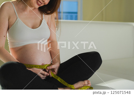 Pregnancy motherhood. Pregnant woman measuring big belly. Girl measuring her belly with tape to keep track of her fetus development. Woman enjoying pregnancy. Maternity tenderness parenthood new life 125071548
