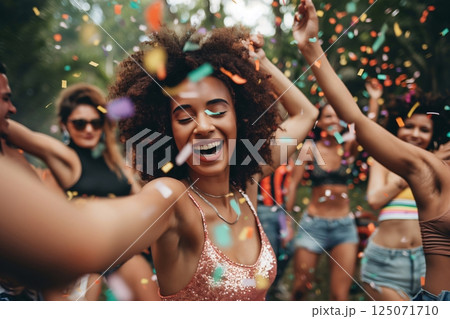 Young woman with afro hairstyle laughing and dancing with friends at a music festival with confetti falling 125071710