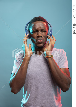 Male influencer with wireless headset, enjoying beautiful sounds and feeling the rhythm. Black man wearing headphones, immersed in his favorite song, listening against isolated background. 125072102