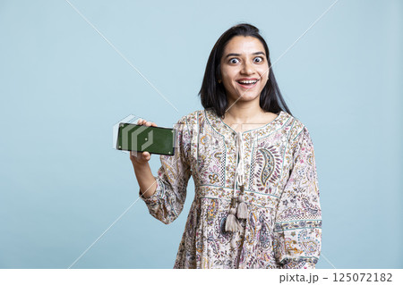 Confident woman presenting green screen on mobile gadget, standing against studio background. Cheerful indian person holding copy space chroma key smartphone used for advertising brands. Confident woman presenting green screen on mobile gadget, standing against studio background. Cheerful indian person holding copy space chroma key smartphone used for advertising brands. 125072182