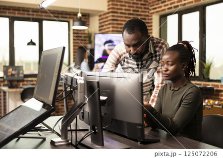 Serious african american colleagues analyzing a startup project on a desktop monitor in a startup company. Determined black creative professionals working together at computer, refining designs. 125072206